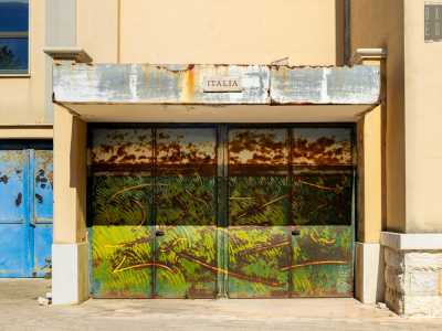 Ed eccoci finalmente davanti a Porta Italia. Fu Milvia Maglione, artista che mescolava Surrealismo e Pop Art, a raffigurare un verde prato illuminato dal sole mediterraneo, che si stagliava su un mare blu sullo sfondo